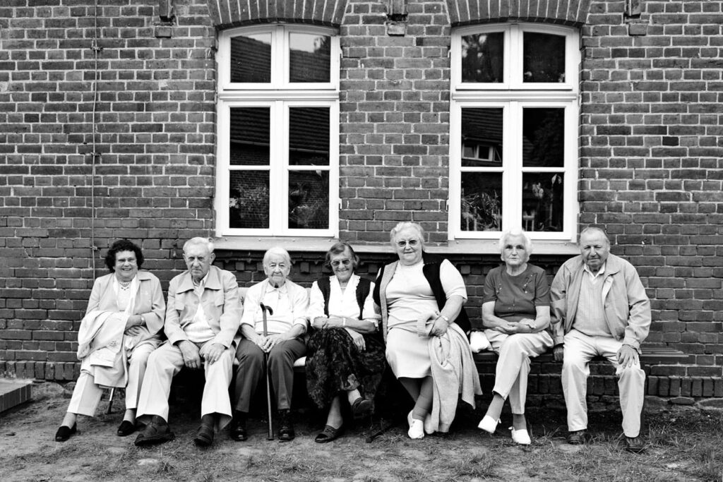 Gruppe älterer Menschen auf Bank vor Backsteinhaus – Dorfgemeinschaft und Generationen im ländlichen Raum
